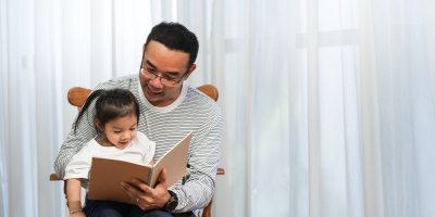 Asian dad reading bedtime story to his daughter