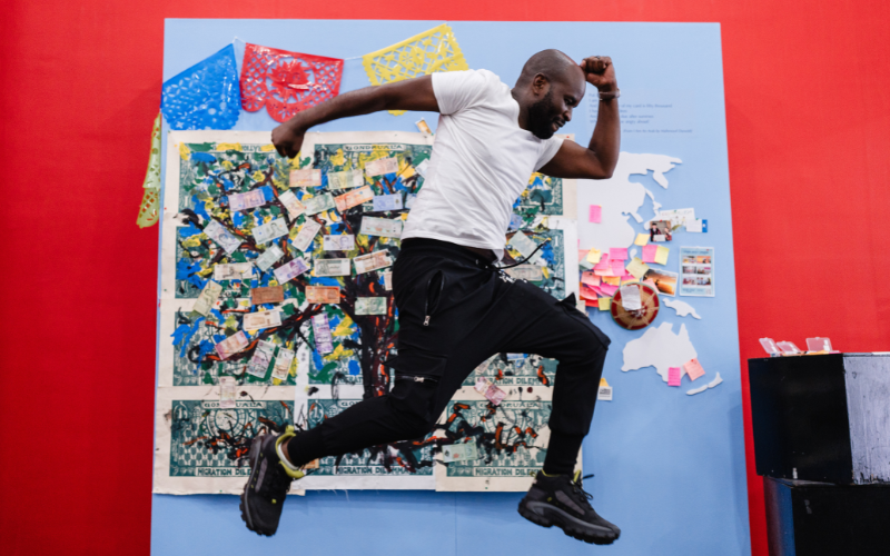 A participant posed at the "Think of Others" activity booth, featuring the artwork from "Money Tree: The Currency of Migration" session.