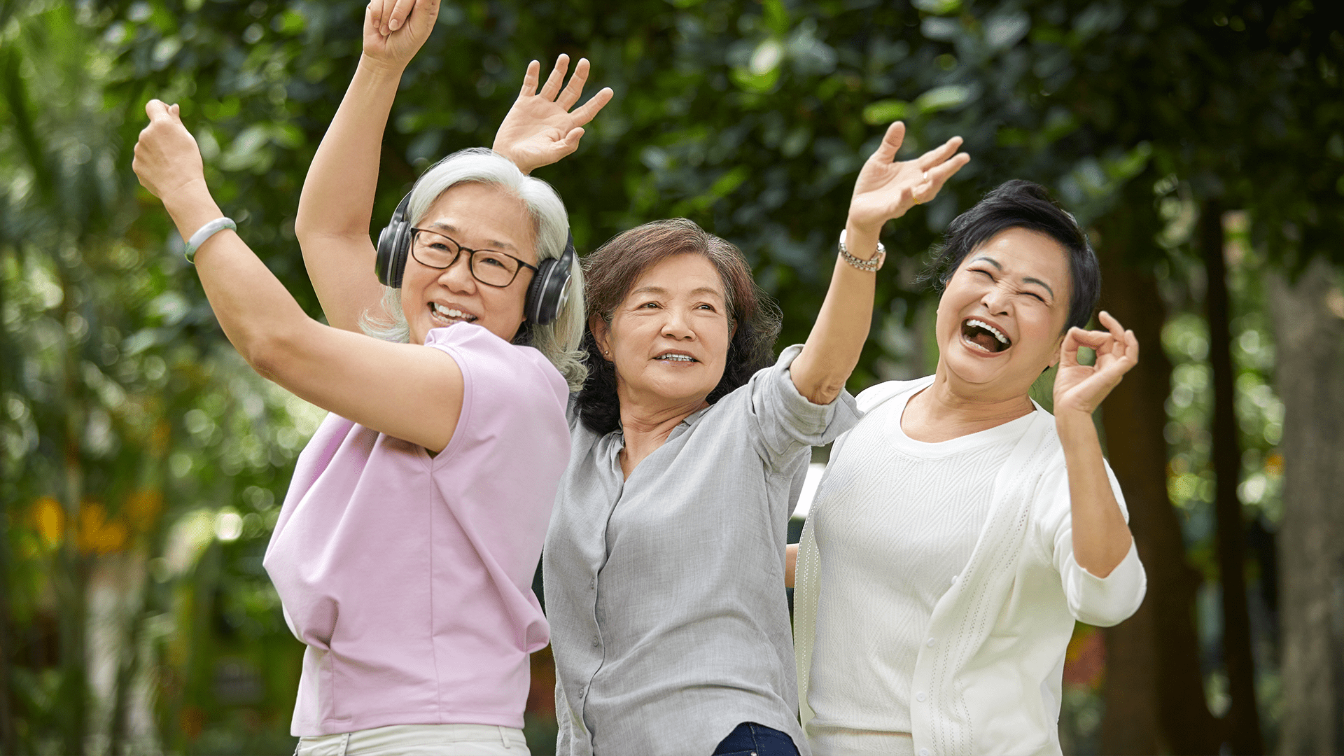 Three joyful senior women celebrating outdoors, surrounded by nature. Their genuine smiles and vibrant energy showcase the beauty of friendship and living life to the fullest.