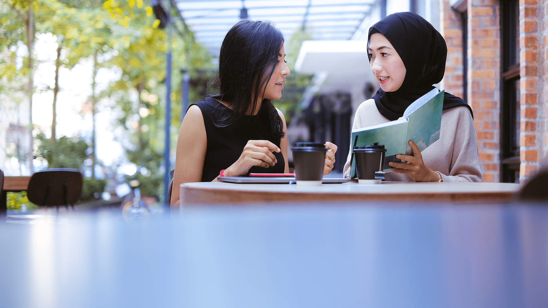 A chinese and malay female sitting outside the cafe, discussing on some ideas presented in the book