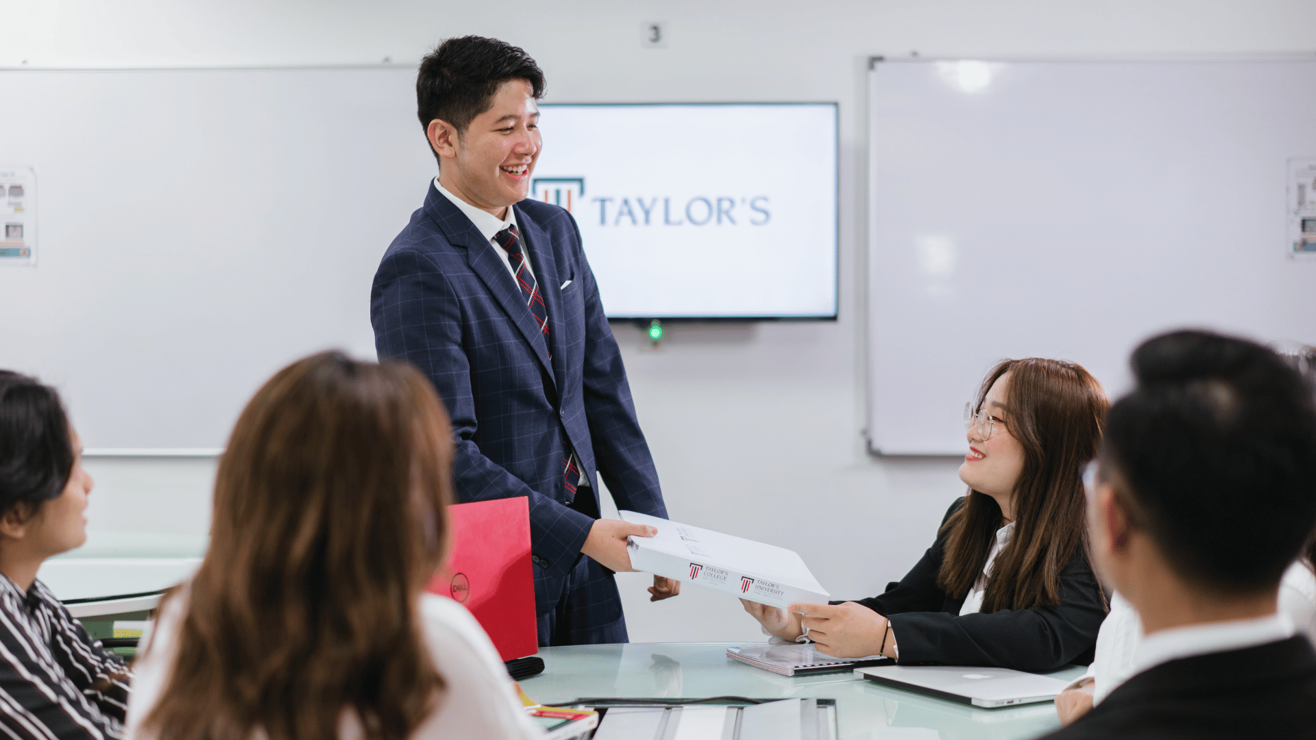 Man handing a document to a woman during a meeting at Taylor’s.