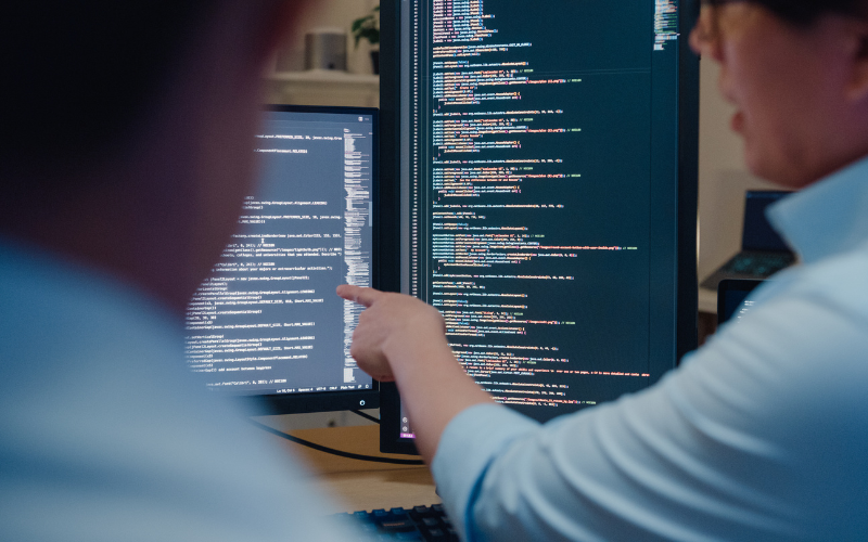 men talking over lines of code on a screen