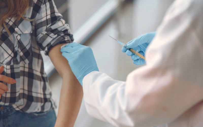 A healthcare professional in a white coat and blue gloves prepares to administer a vaccine to a patient's arm, capturing a moment of healthcare in action.