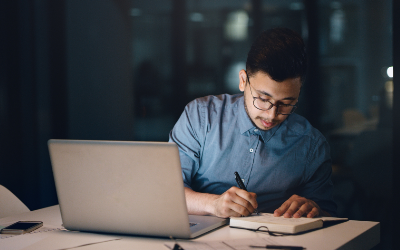 Guy writing notes beside laptop