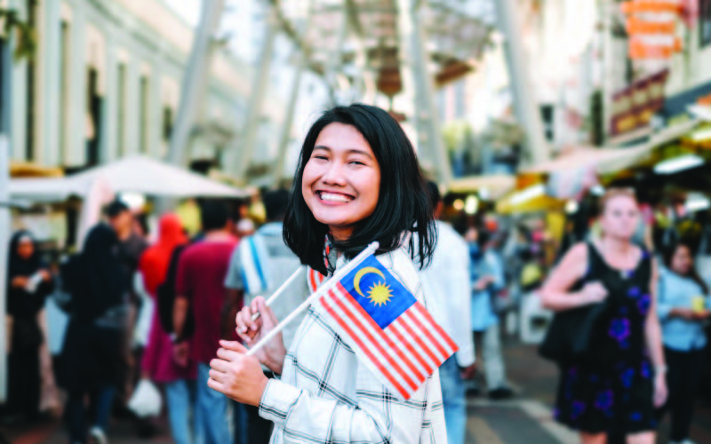 A smiling Malaysain student holding up Malaysian flags abroad