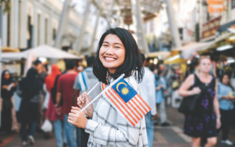A girl in busy Petaling Street Showing her patriotism by holding two Malaysian flags