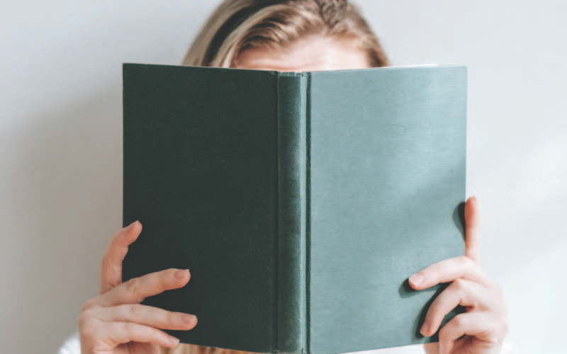 A girl holding an opened book up and covering her face.