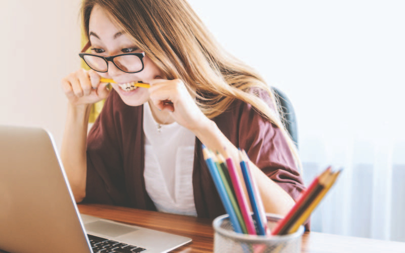 Student stressed biting their pencil in front of laptop