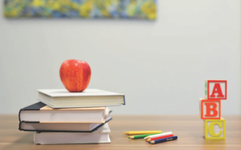 An apple on a stack of books with alphabet building blocks on the side.