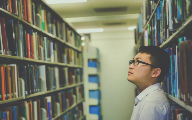 A man in a library looking at the different books on the shelves.