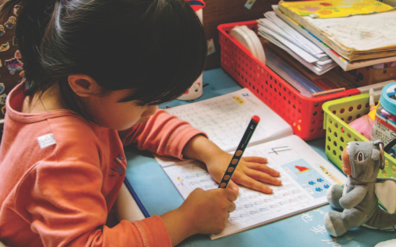 A young child practising her motor skills development by writing the number 4 in a workbook.