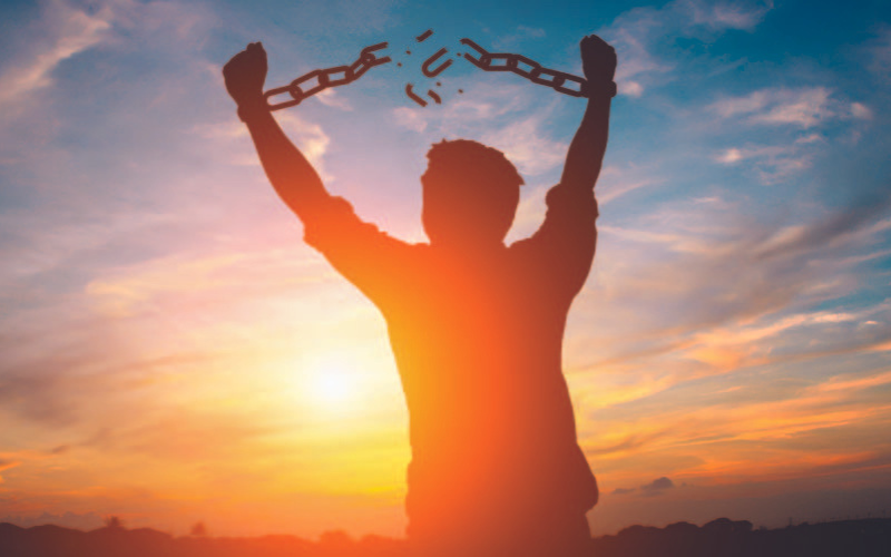 A silhouette of a guy breaking his chain holding him back with a view of a sunset.