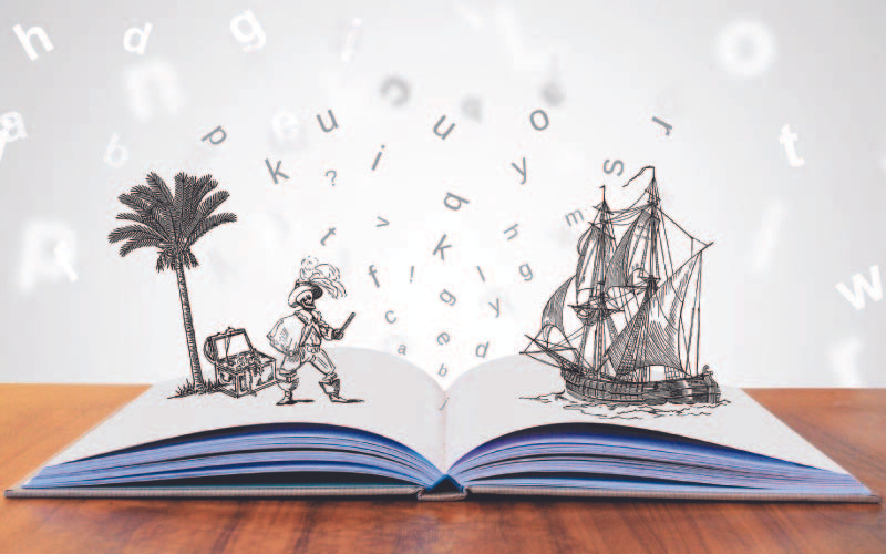 An open book on a table with imaginative illustrations: a pirate and treasure on the left and a ship on the right, with floating letters above. The background is blurred, suggesting an indoor setting.