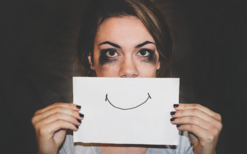 A girl, with mascara smeared under her eyes, holding up a piece of paper with a smile
