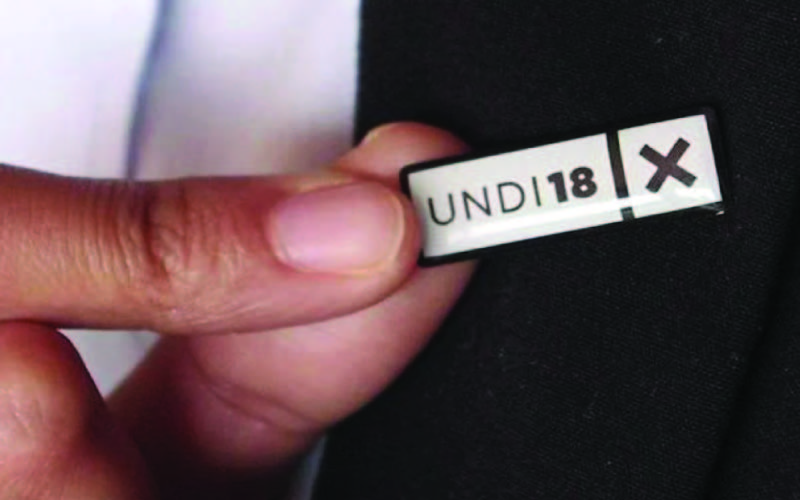 A person showing an 'UNDI18' tag on a jacket