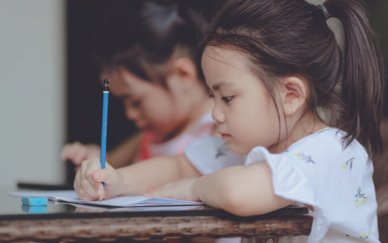 Two young children focused on writing in notebooks at a table.