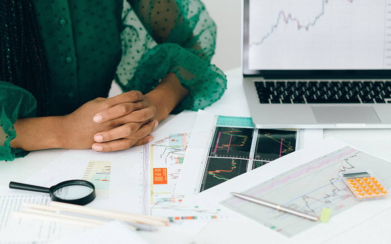 person sitting at a desk with charts, graphs, and a laptop displaying financial data