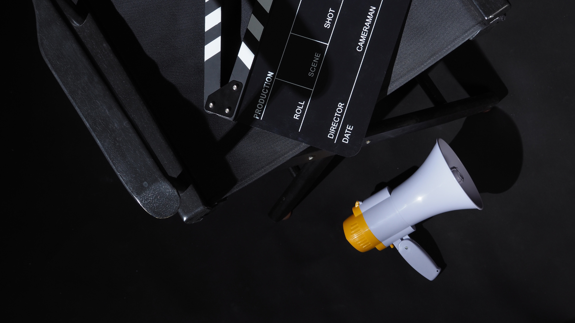 A black clapperboard on a director’s chair, next to a white megaphone on the floor