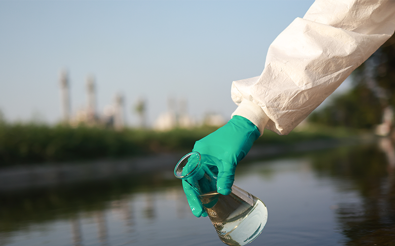 Close-up scientist or environment engineer's hand with a chemical protective suit and PPE collect a sample of toxic wastewater from a chemical flask