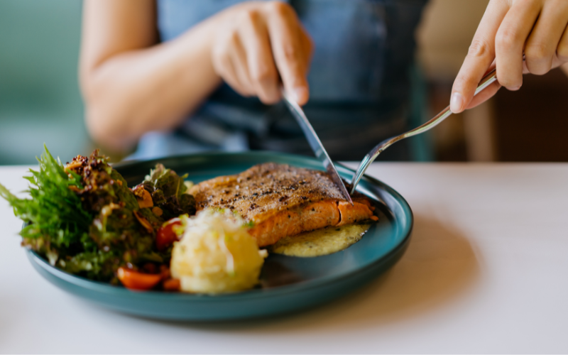 Hands cutting into a salmon dish
