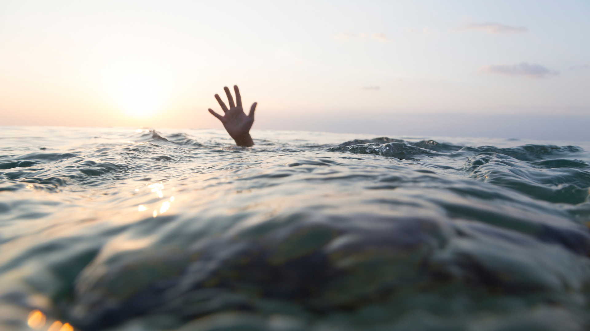 A person drowning, their hand rising from the ocean