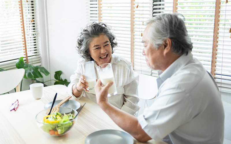 Asian Senior Adult couple holding glasses of milk together at home
