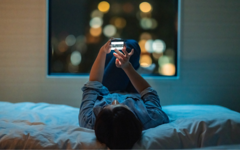 Woman lying on her bed, scrolling her phone