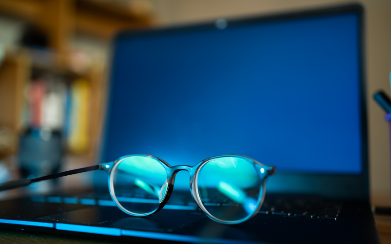 A pair of glasses rests on the keyboard of a laptop with a blue screen