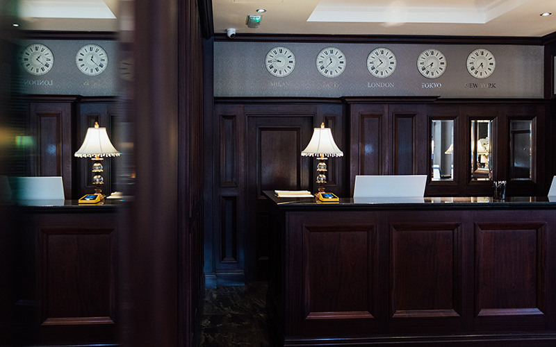 A dark wood hotel reception desk reflected partially in a mirror