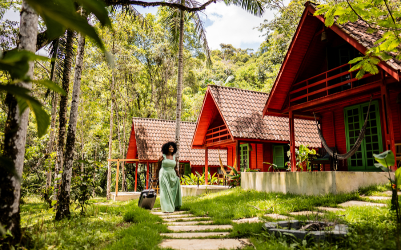 A woman with a suitcase approaching eco-lodges surrounded by greenery