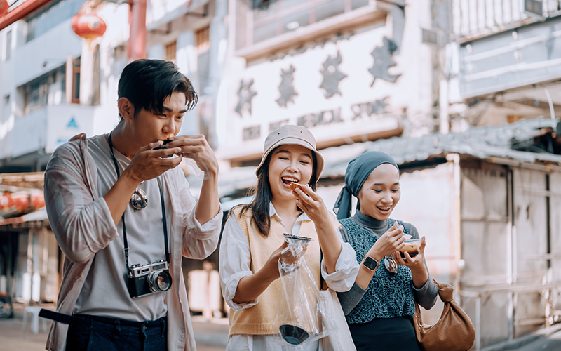 Group of Asian young travelers trying local street food at Petaling Street Chinatown street market