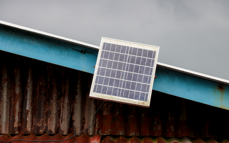 A small solar panel mounted on the rusted roof of a weathered building