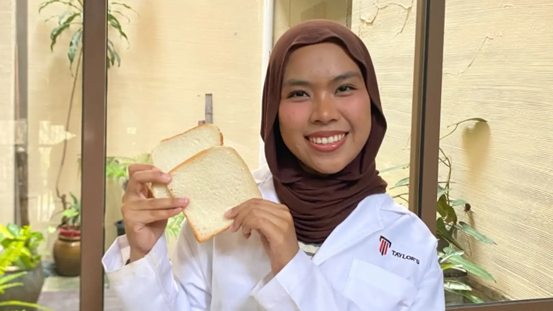 Ayesha Mohd Ibrahim in a Taylor's lab coat, smiling and holding up two slices of white bread