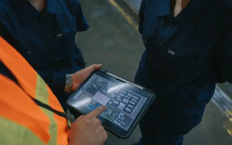 Engineers in work uniforms reviewing system data on a tablet on a factory floor