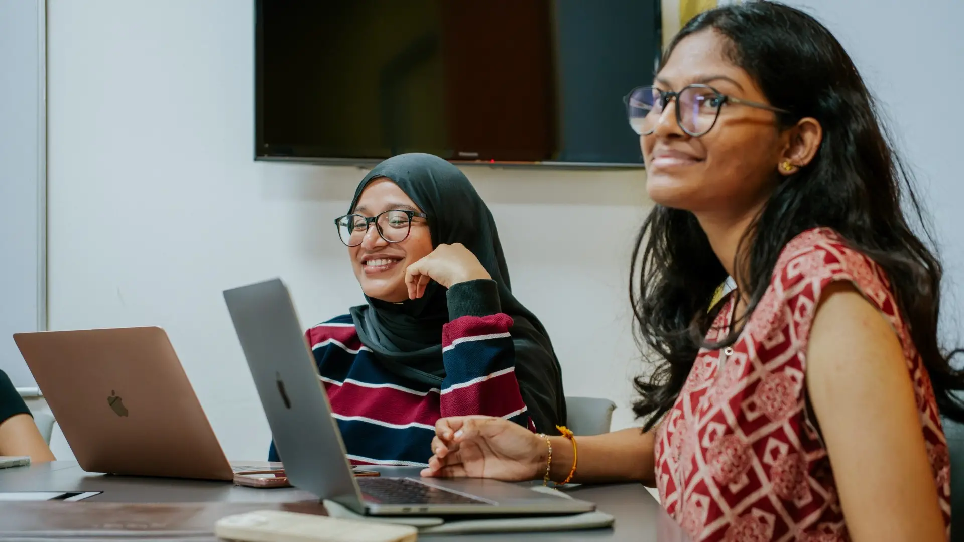 Two postgraduate students smiling during a class discussion with laptops at Taylor's University