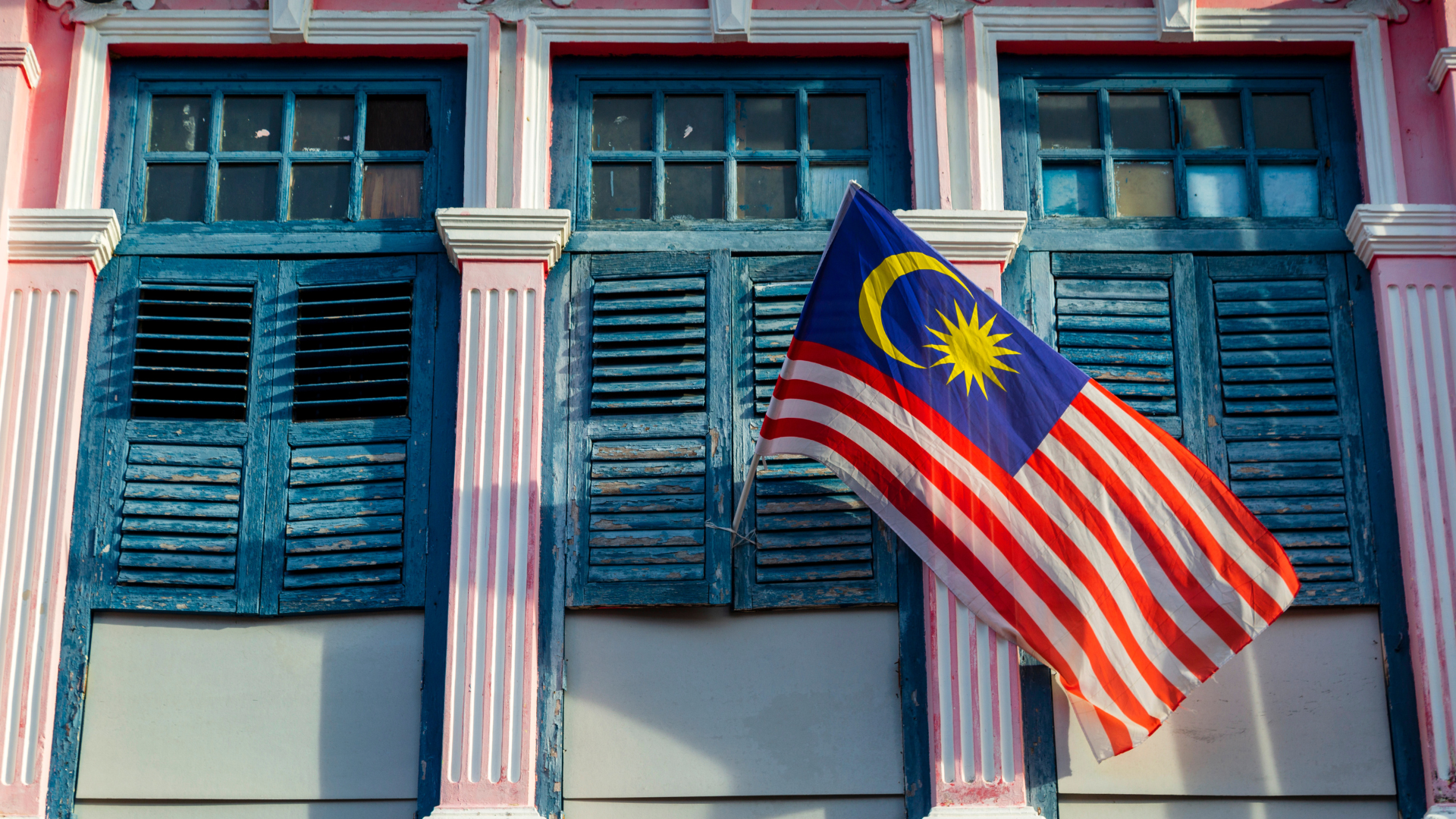 The Jalur Gemilang, fastened between two weathered shutters on a heritage shophouse façade