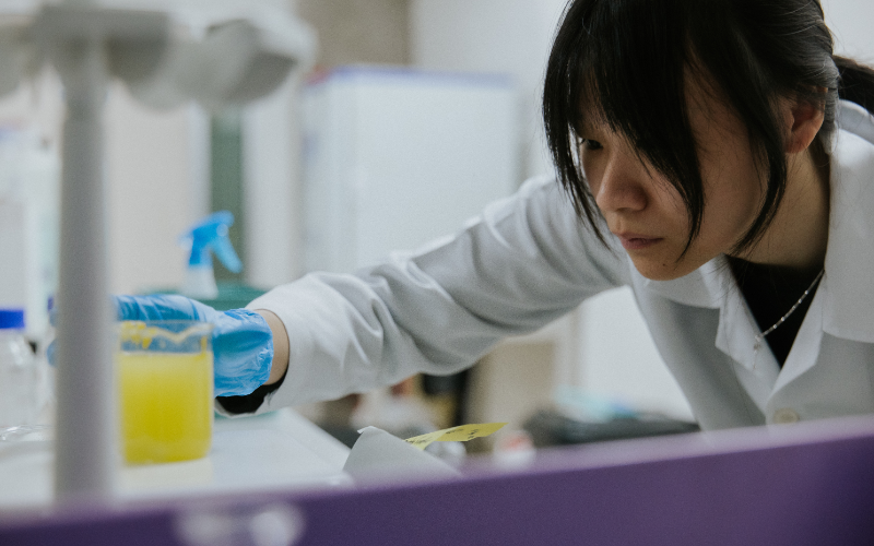 Researcher in a lab coat handling a beaker of yellow solution at a laboratory bench