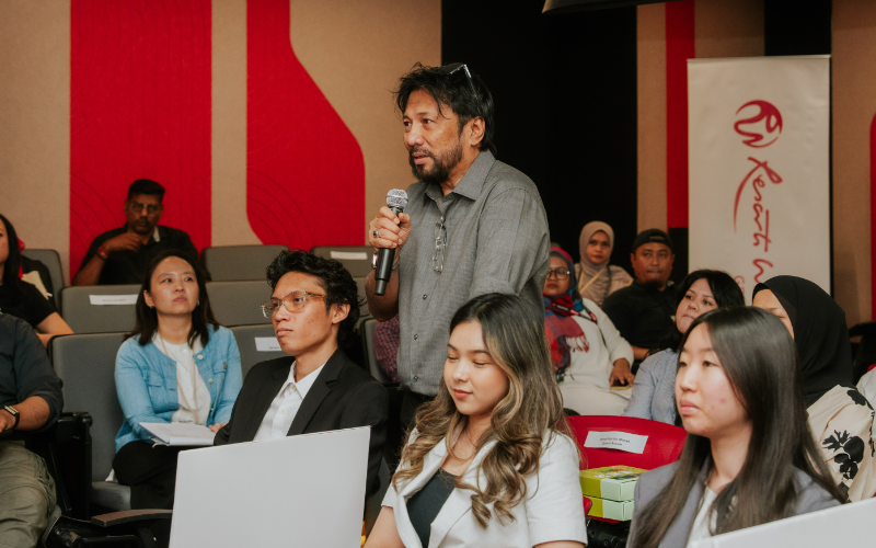 Audience member standing with a microphone to ask a question at a forum at Taylor's University