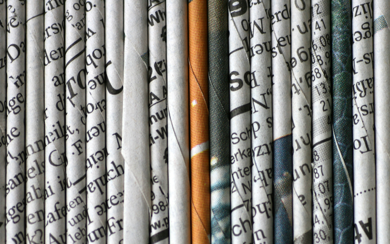 Rows of folded newspapers stacked on edge, showing printed headlines and text