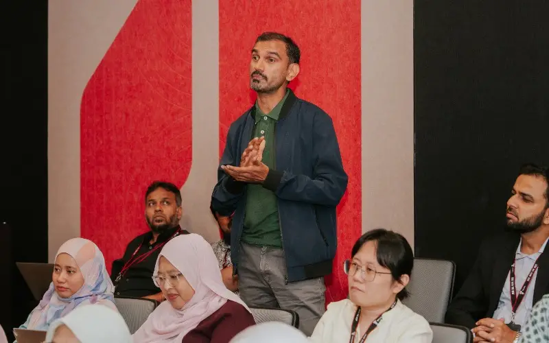A participant in a navy jacket stands to put a question to the forum panel