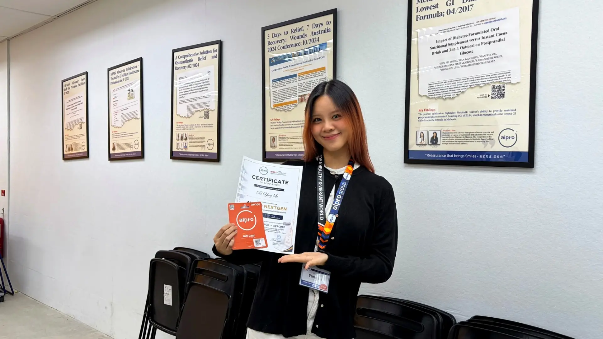 Celeste holding her Alpro NextGen certificate and an Alpro gift card in front of framed research posters
