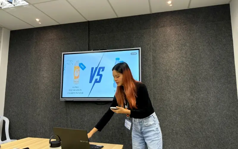 Celeste presenting her product pitch beside a screen comparing two bottled water products