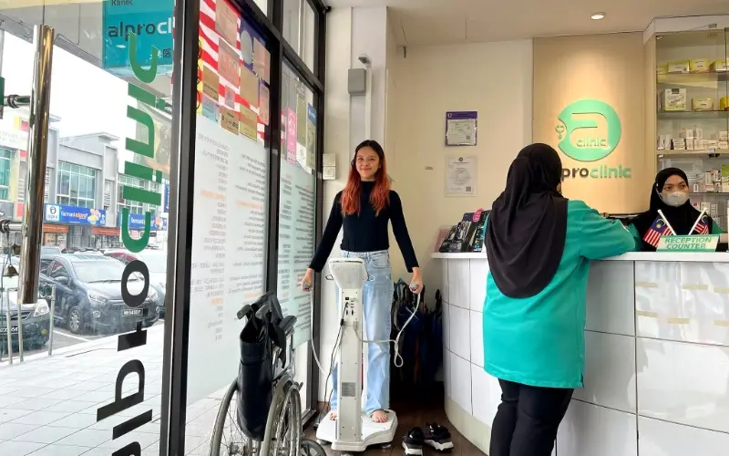 Celeste standing on a body composition analyser inside Alpro Clinic, beside the reception counter