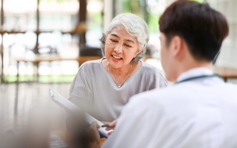 A happy Asian old lady or grandmother is being checked on by a doctor and talking about health treatments with a doctor in an examination room at a hospital.