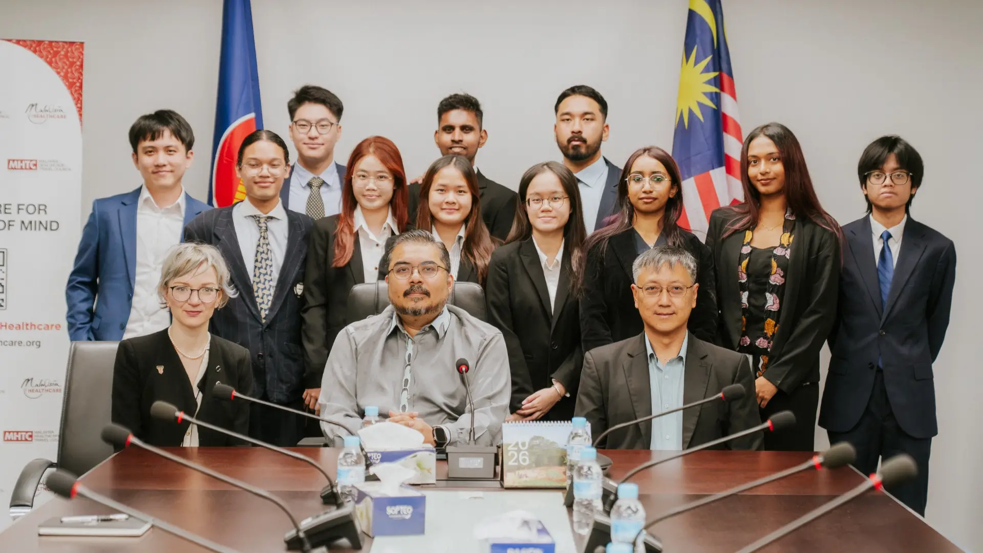 The Taylor's student delegation and their hosts in a group photo in a meeting room, with the ASEAN and Malaysian flags behind them