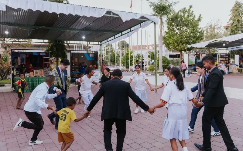 Taylor's students holding hands with local schoolchildren in a circle game in a courtyard in Timor-Leste