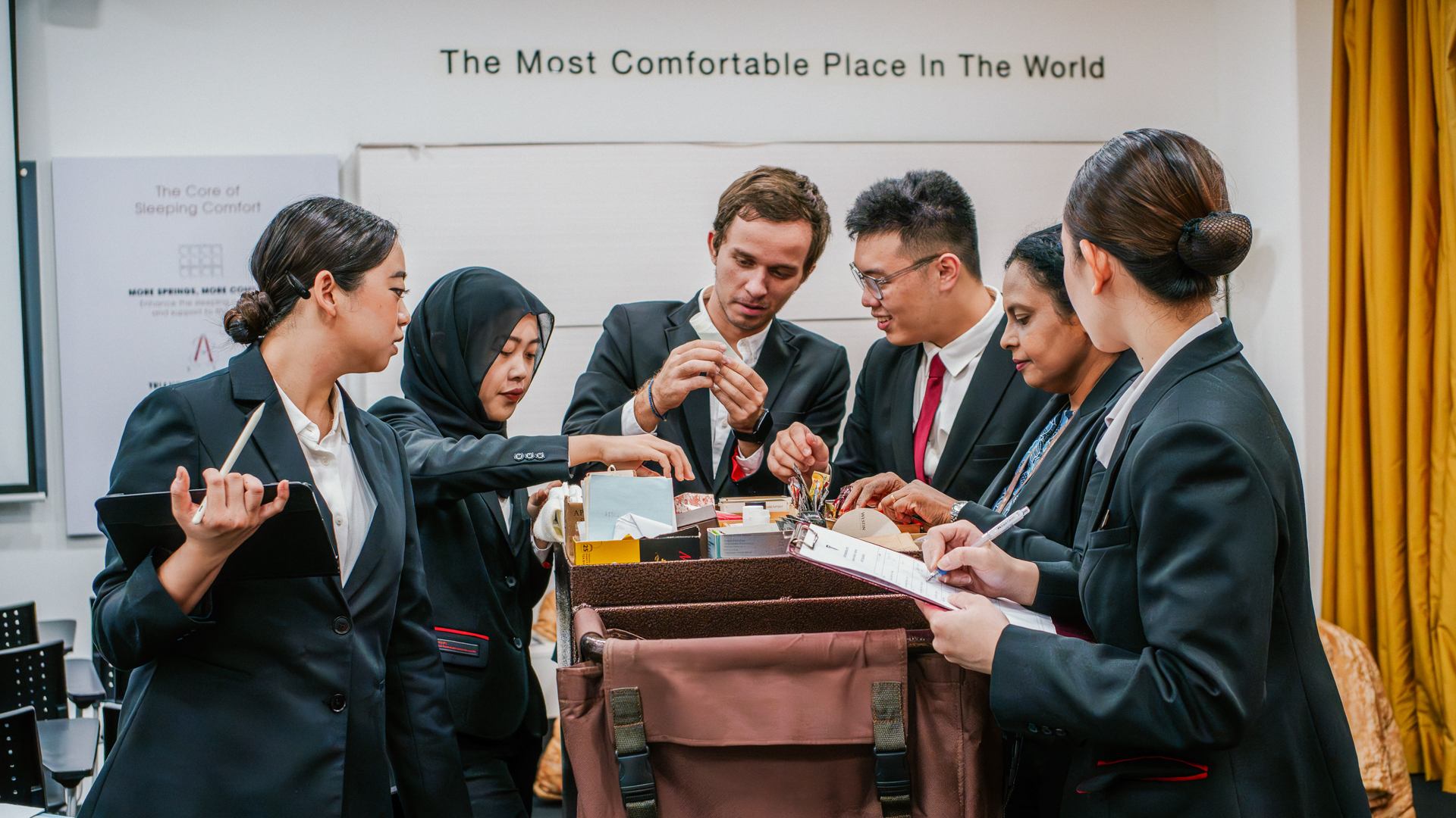 Taylor's University hospitality students in professional suits collaborating on a practical management exercise in a modern training environment.