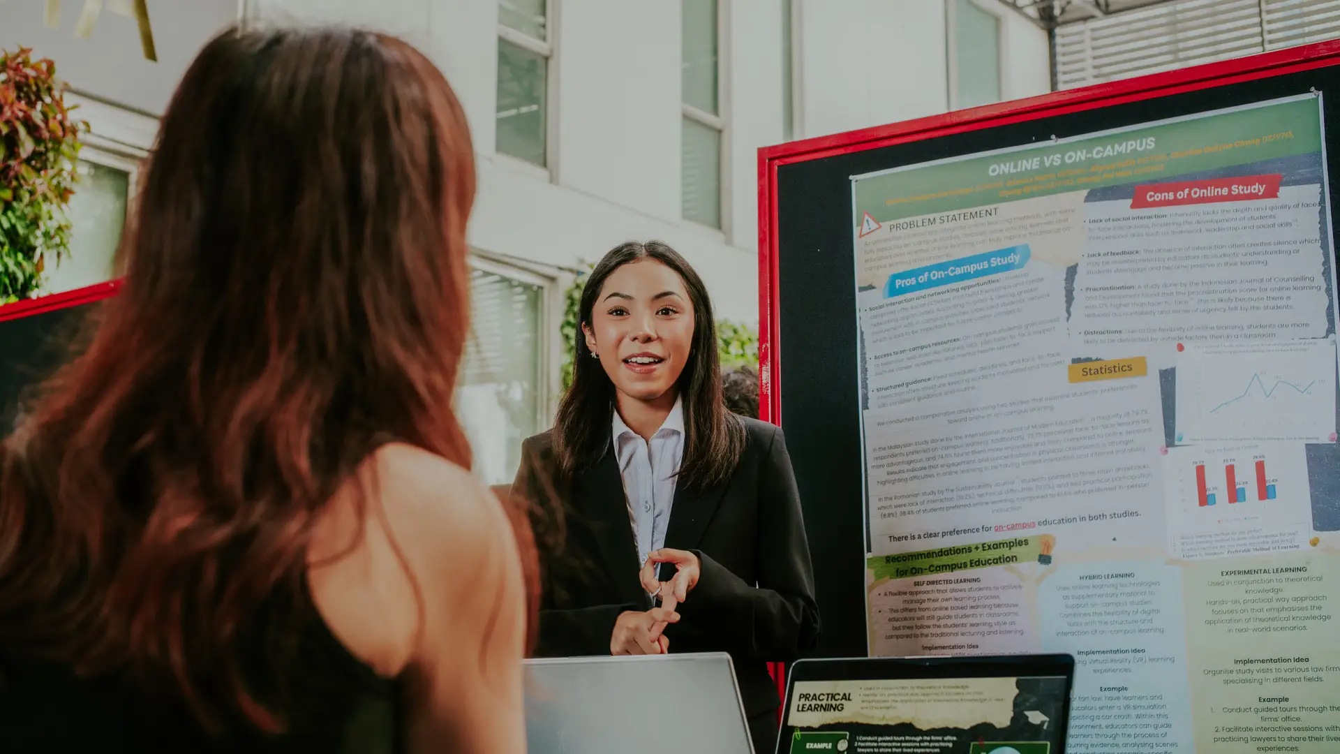 A Taylor's University student in professional attire presenting an academic poster during an interactive campus showcase