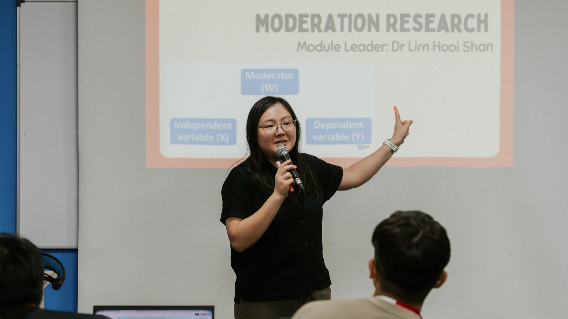 A lecturer gives a presentation while speaking into a microphone in front of an audience.