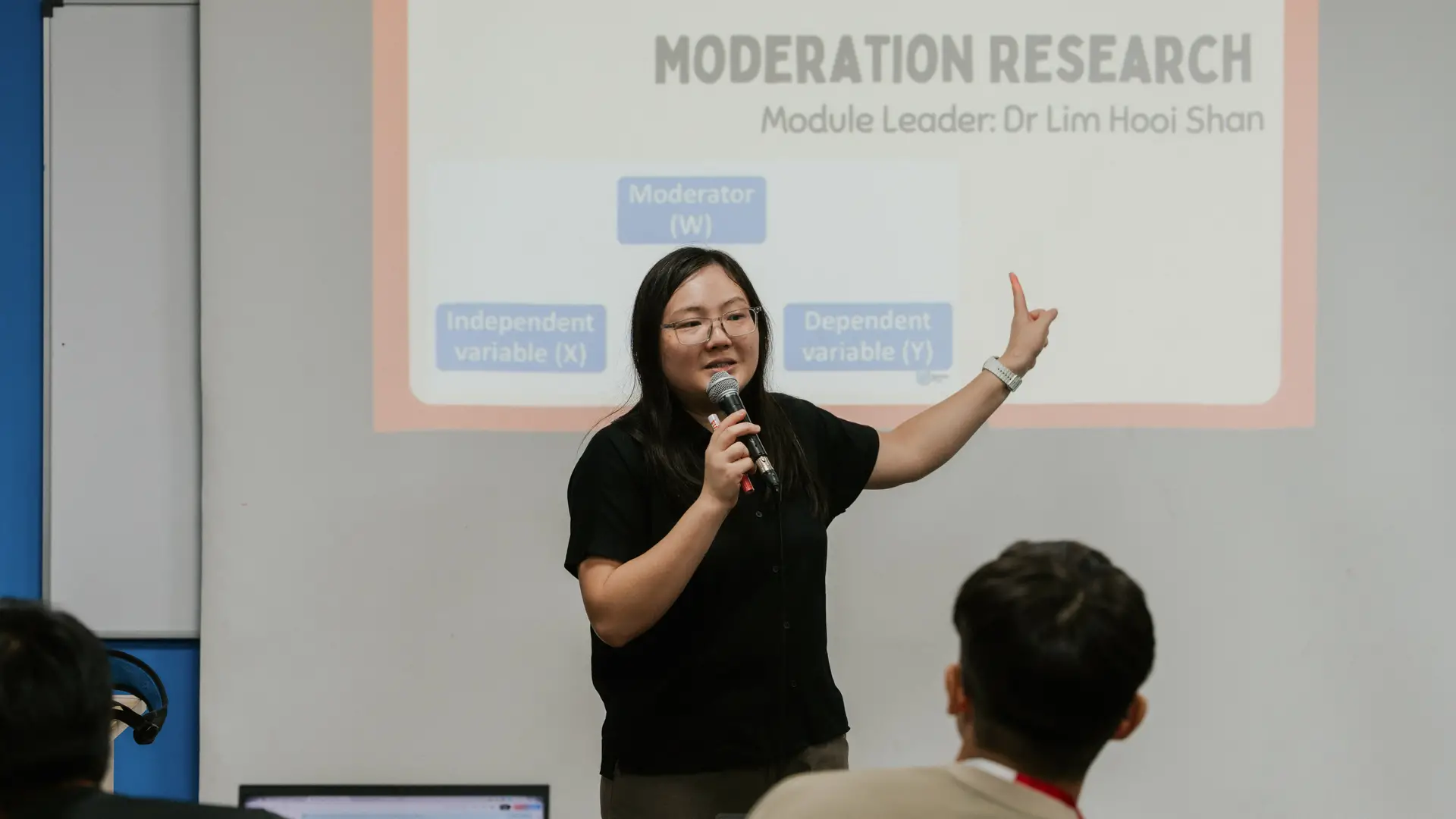 A lecturer gives a presentation while speaking into a microphone in front of an audience.
